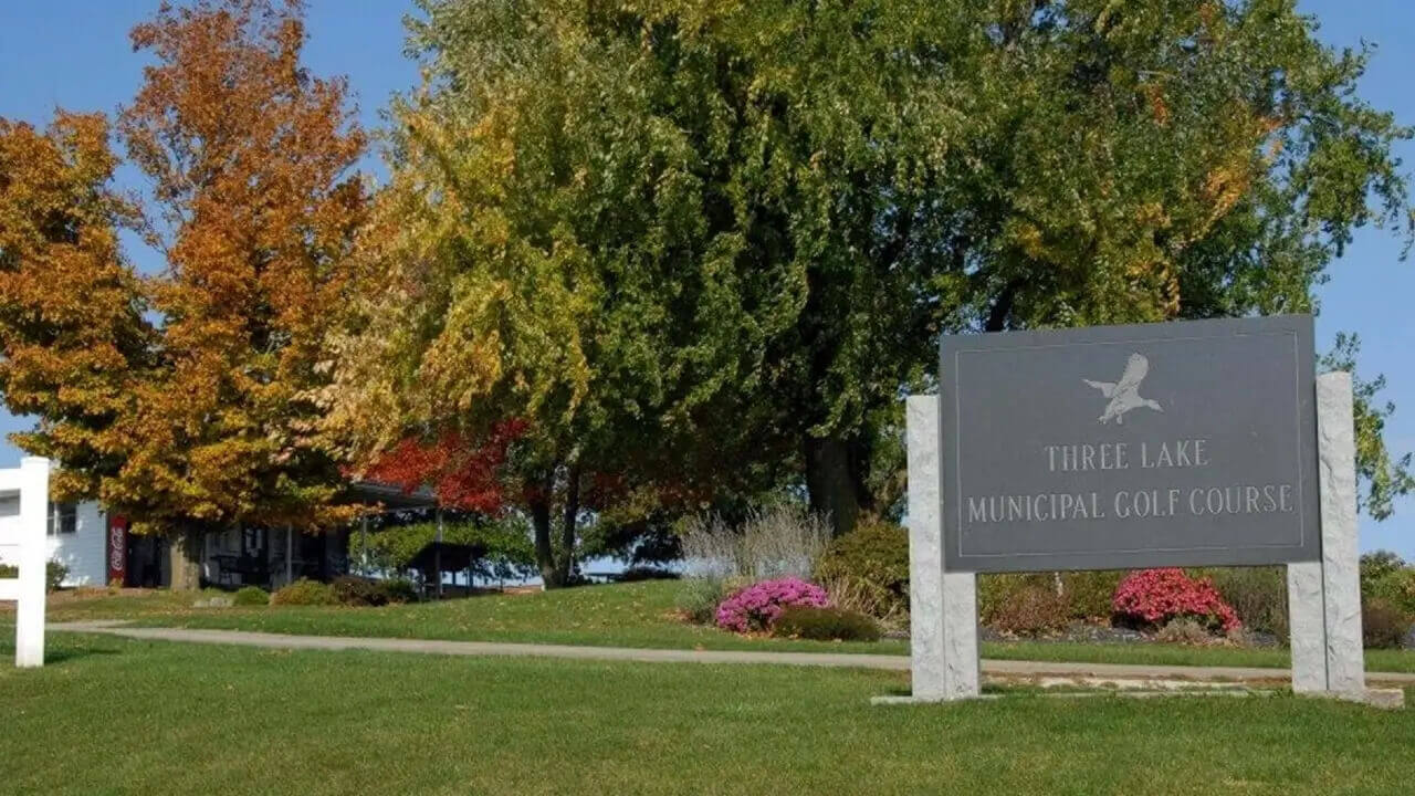 A scenic view of a lush green golf course entrance in Lenox, Iowa, during early afternoon.