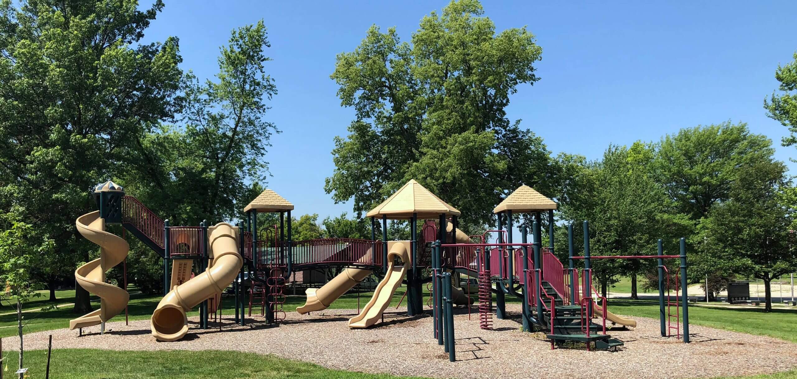 A vibrant landscape of a modern city park with manicured green lawns and a state-of-the-art playground under a clear blue sky.